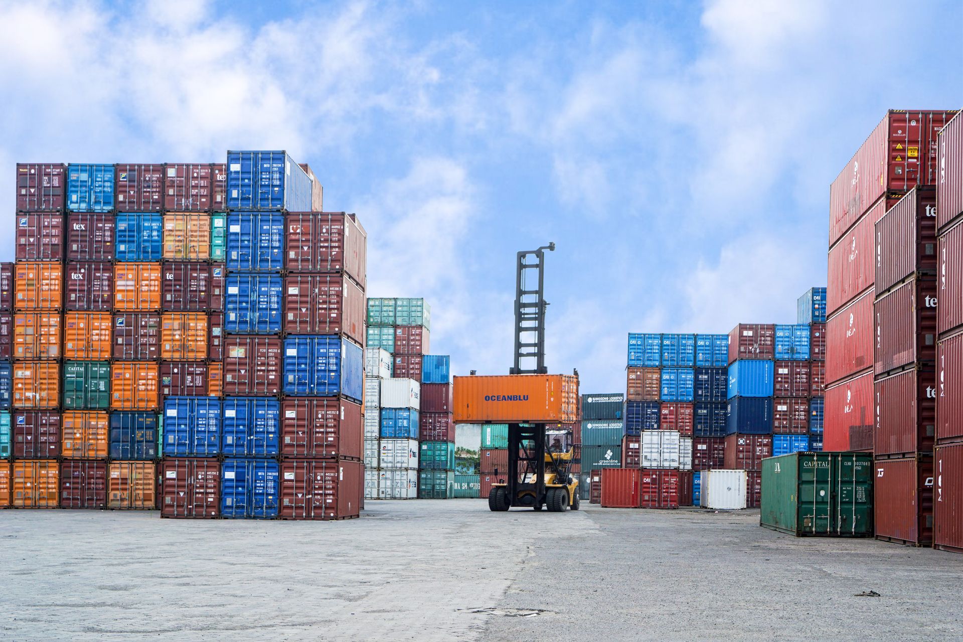 Containerterminal mit Umschlaggerät und gestapelten Seecontainern unter klarem Himmel